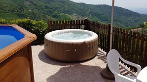A hot tub with an orange umbrella, surrounded by a wooden fence, and a pool, with a mountainous landscape in the background. - Amelia Hotel (Marliana)