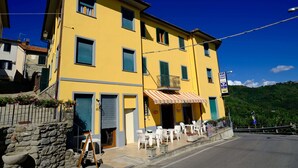 A yellow building with a bar sign, outdoor seating, and a stone wall. - Amelia Hotel (Marliana)