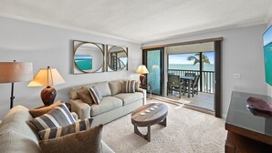 A living room with a sofa, two lamps, a coffee table, and a view of the ocean through a sliding glass door.