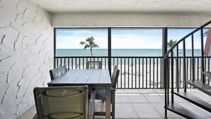 A balcony with a table and chairs, overlooking a beach with palm trees and the ocean.