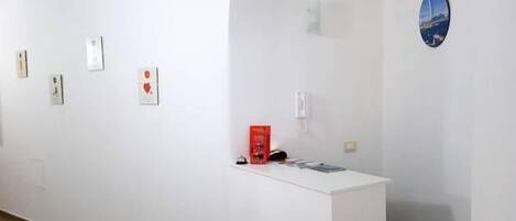 A gallery with white walls, a wooden floor, and a curved ceiling. There are artworks displayed on the walls and a small table with a red box and some items on it.