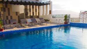 A pool area with lounge chairs and a view of mountains. - Ale Nhatrang Hotel (Nha Trang)