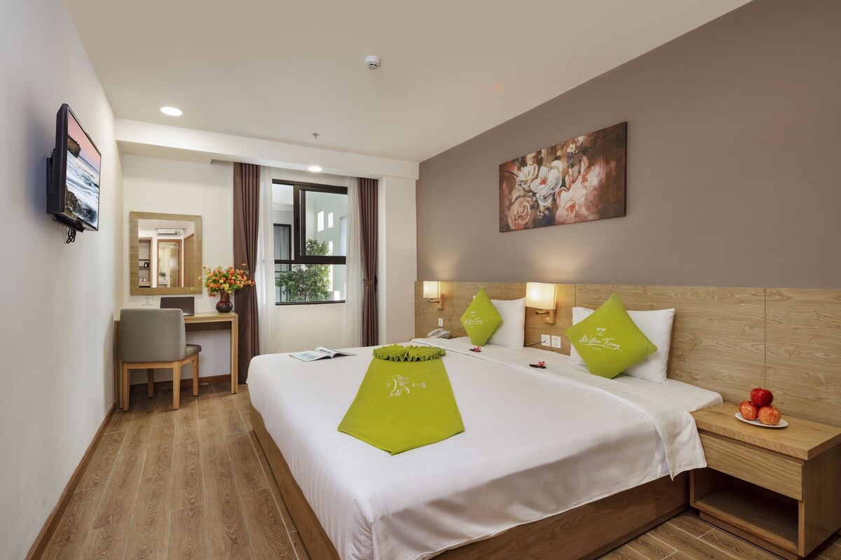 Una habitación de hotel con cama, escritorio, silla, mesita de noche y un cuadro en la pared.