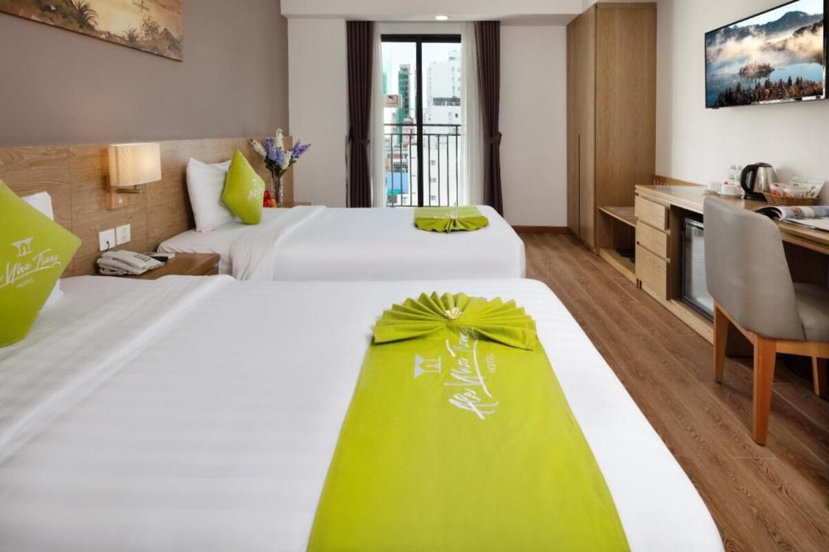 Habitación de hotel con dos camas, un escritorio y vista a la ciudad.
