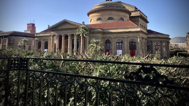 Un edifici gran i antic amb una cúpula i columnes, envoltat de vegetació i una tanca metàl·lica.