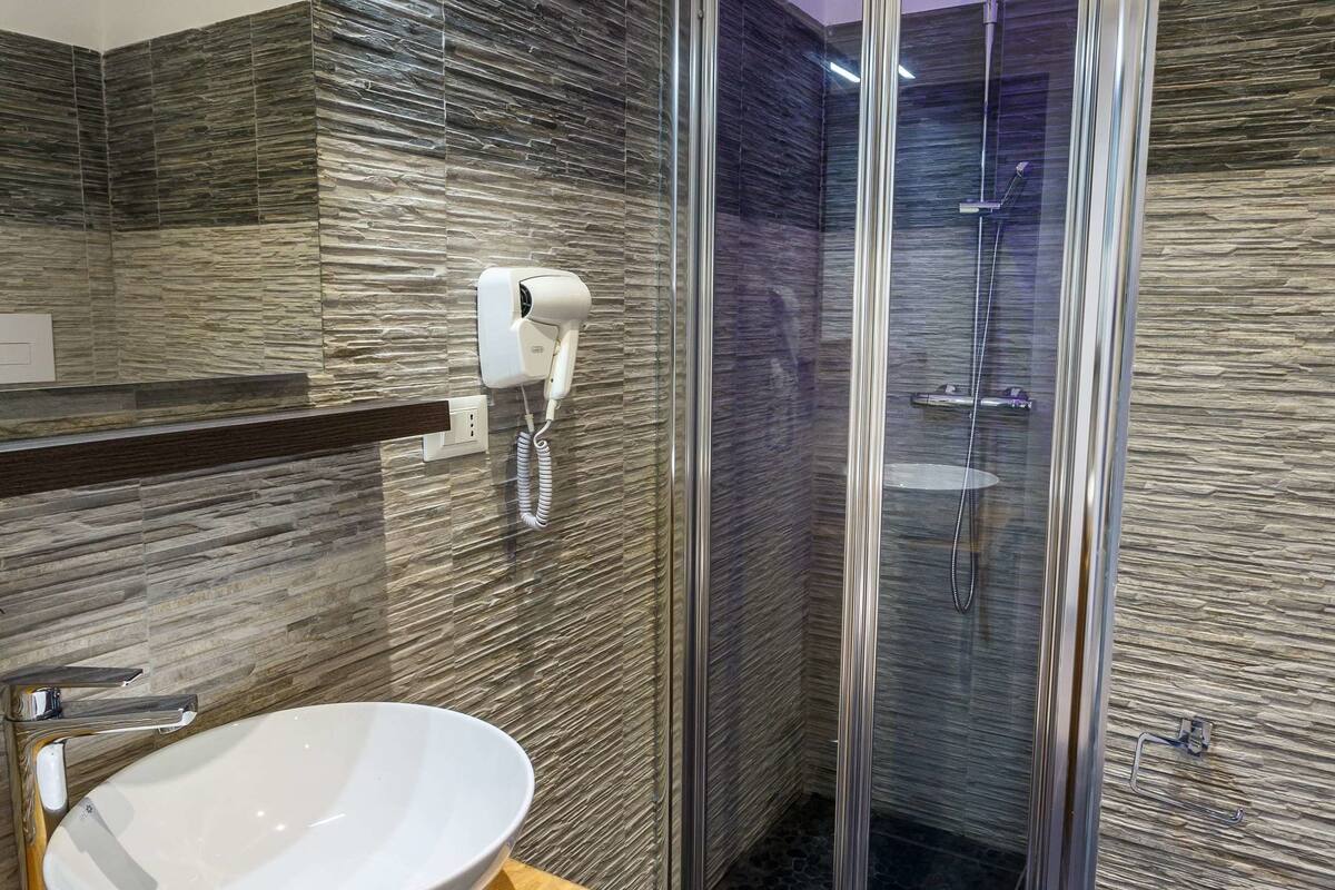 Un baño moderno con ducha de mampara de vidrio, un lavamanos blanco y un secador de pelo en la pared.