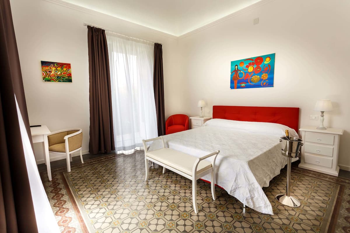 Habitación de hotel con cama, escritorio, silla, mesita de noche y dos cuadros en las paredes.