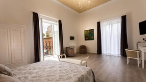 Habitació d'hotel amb llit, escriptori, cadira i un balcó amb vistes a edificis.