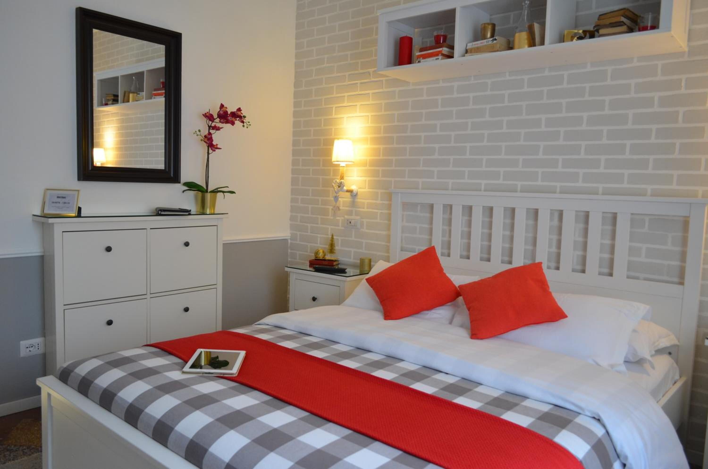 A neatly arranged bedroom with a checkered bedspread, a red throw, and a white headboard.