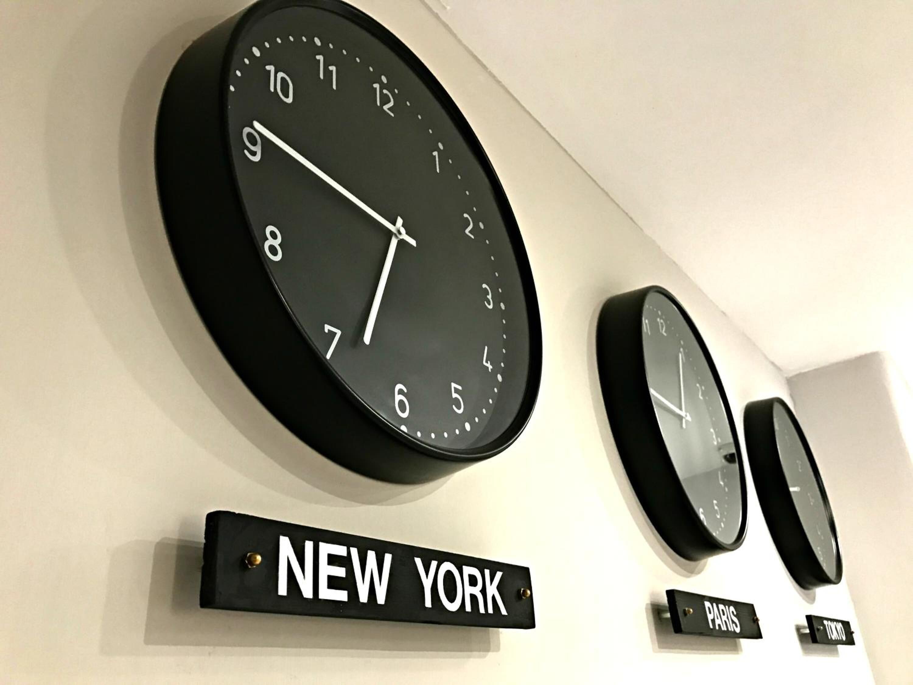 Three clocks on a wall, each with a label below indicating different cities: New York, Paris, and Tokyo.