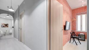 A modern room with a grey and red brick wall, a wooden door, and a TV on a small table. - Moonlight Inn Guest House (Rome)