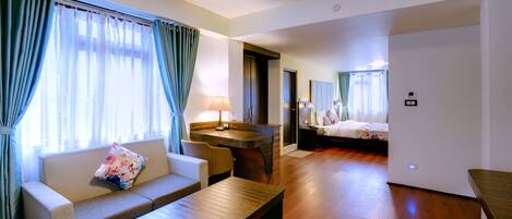 A hotel room with a sofa, a wooden coffee table, a desk, and a bed.