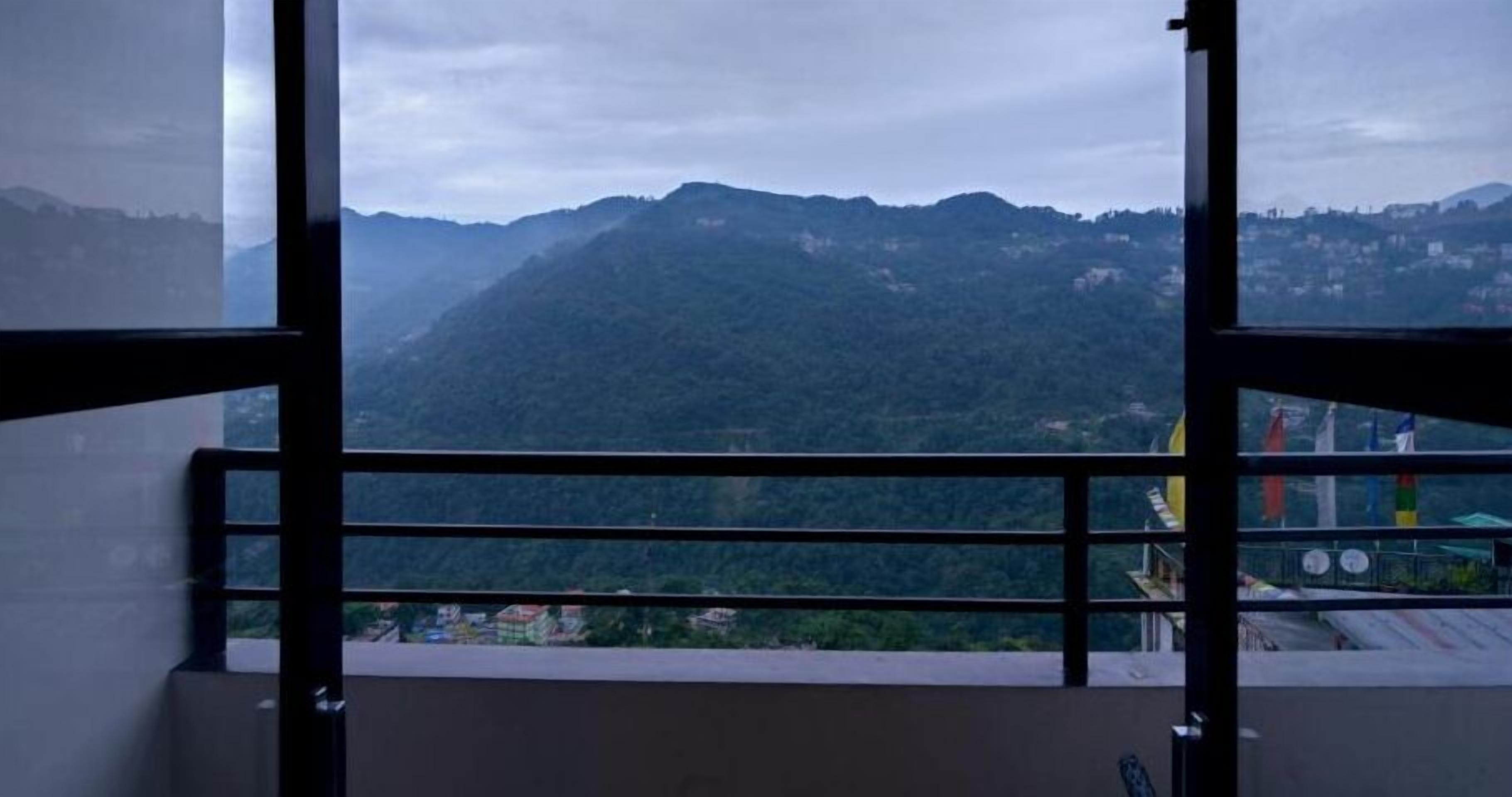 A room with a view of a mountainous landscape through a window with a metal railing.