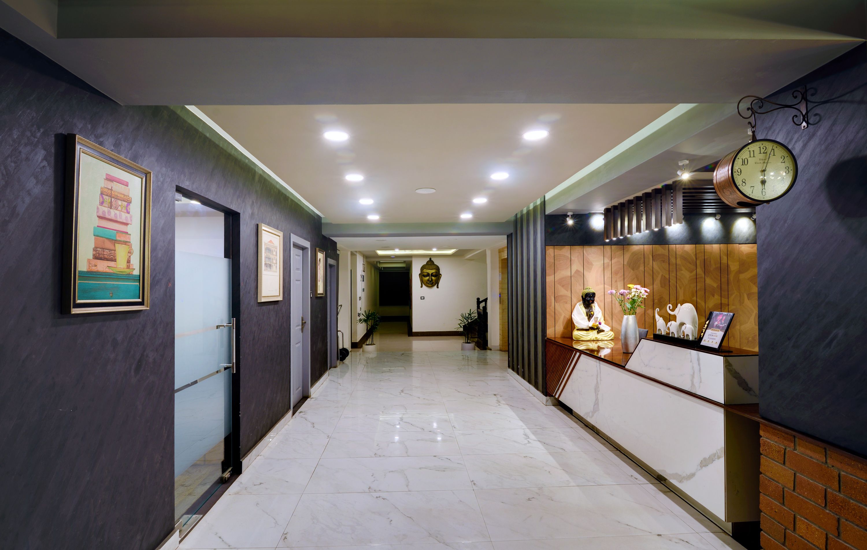 Ein Hotel-Empfangsbereich mit Marmorboden, gerahmten Kunstwerken an den Wänden, einer Buddha-Statue und einer Uhr.