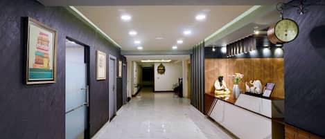 Ein Hotel-Empfangsbereich mit Marmorboden, gerahmten Kunstwerken an den Wänden, einer Buddha-Statue und einer Uhr.