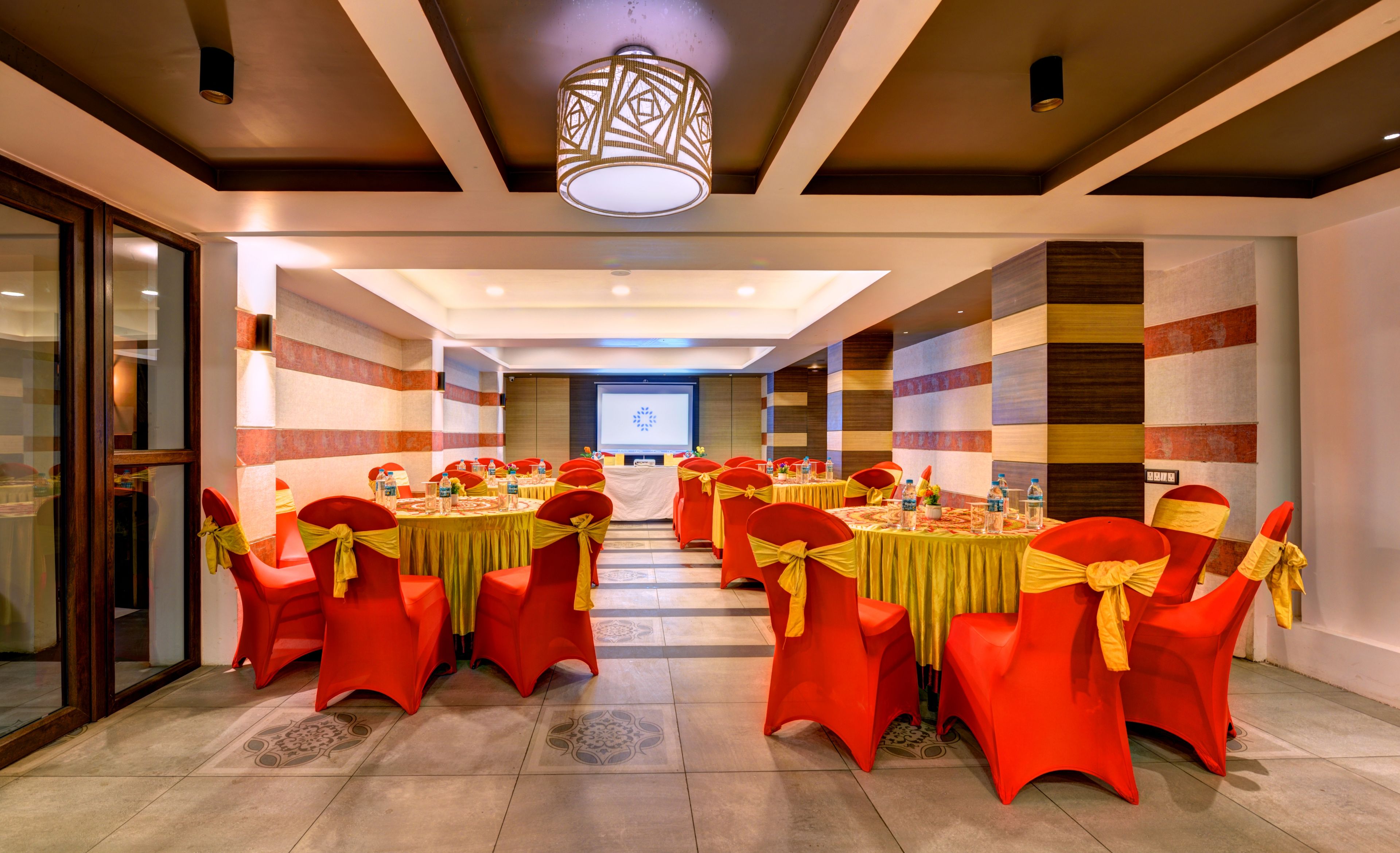 A conference room with red chairs, yellow sashes, and a large screen at the front.