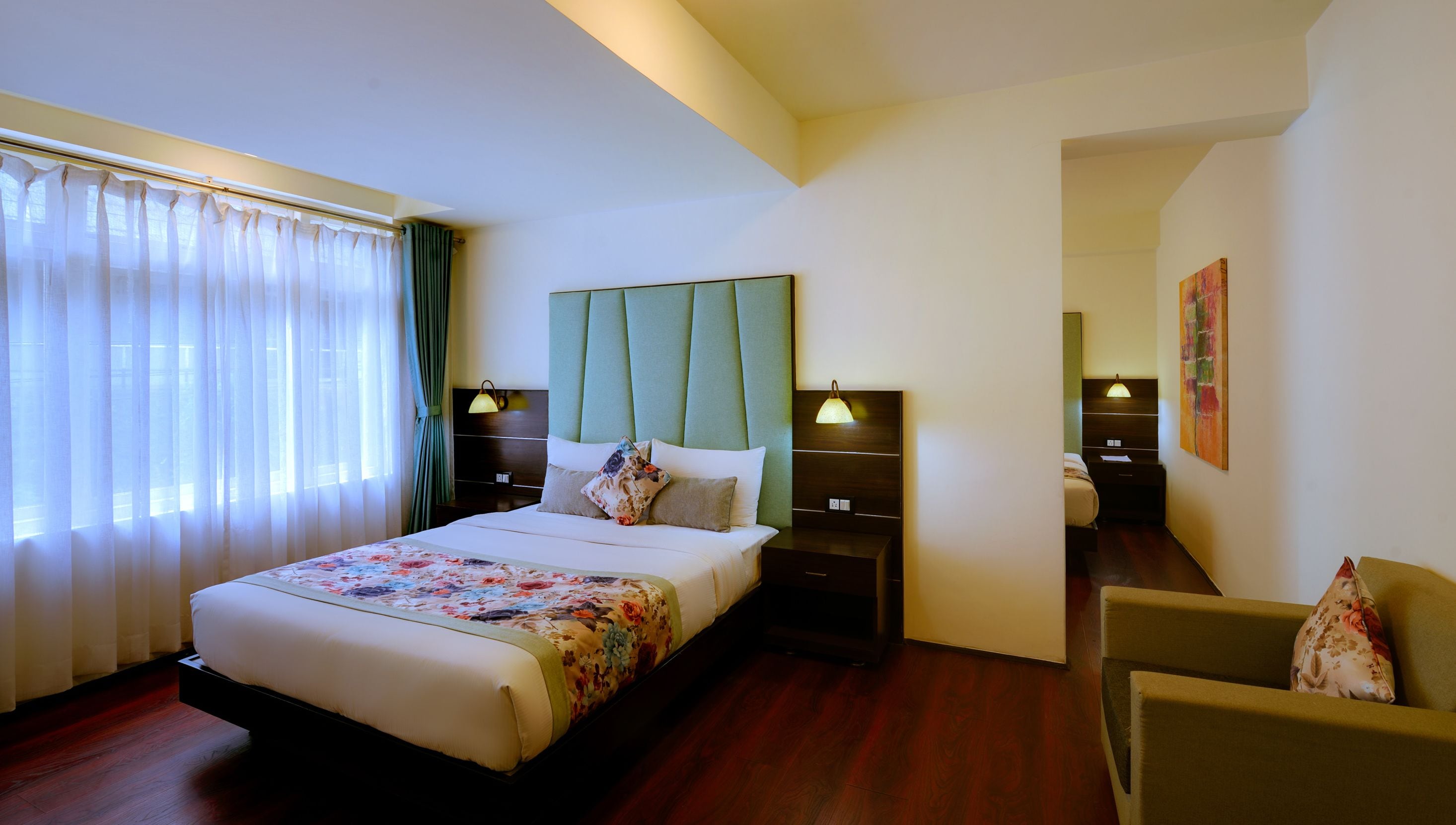 Une chambre d’hôtel avec un grand lit, deux tables de chevet, une chaise, une fenêtre avec des rideaux et un tableau au mur.
