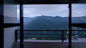 Vista desde una ventana con baranda metálica, que da a un paisaje montañoso con edificios en la base.