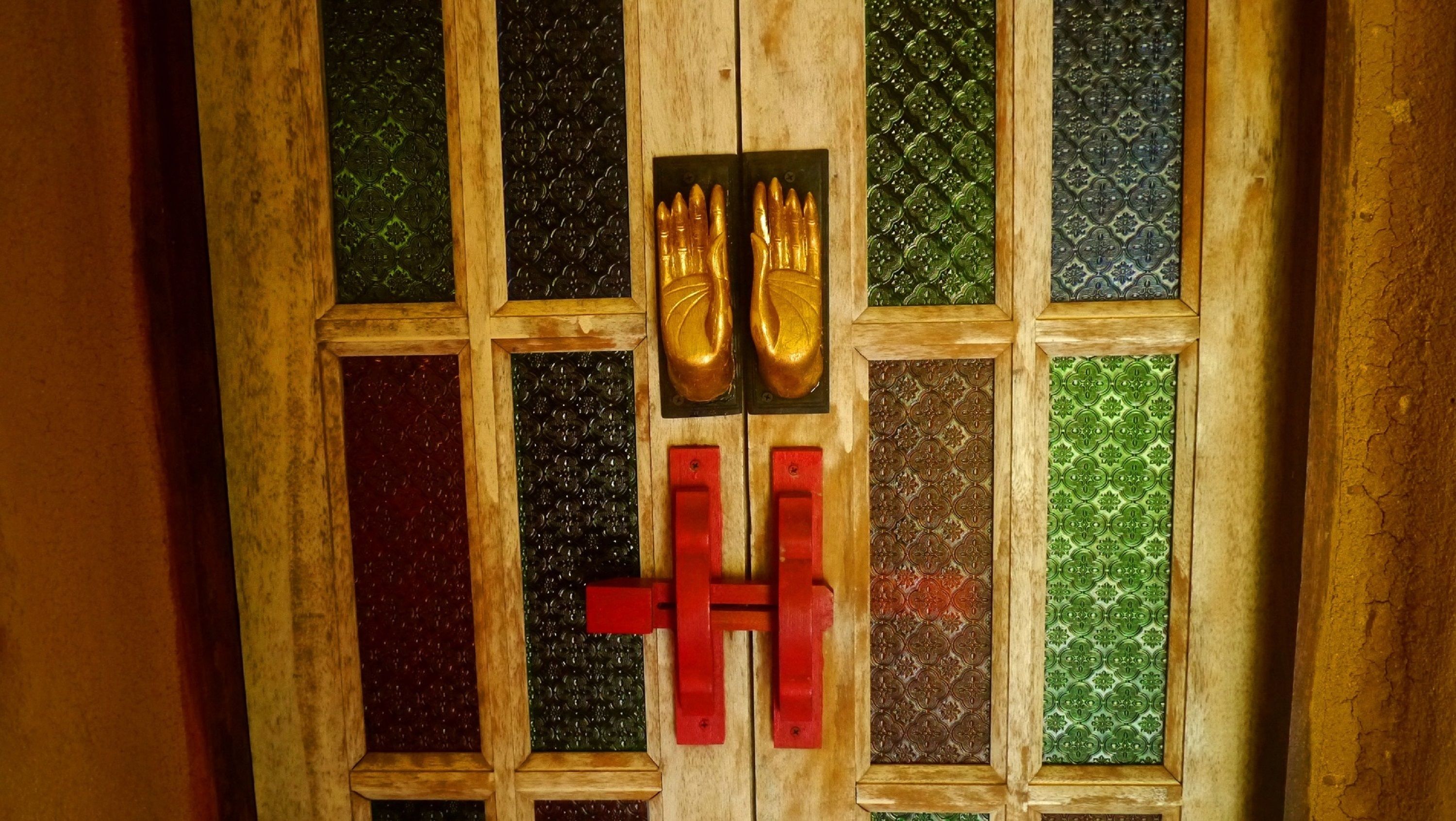 A wooden door with a grid pattern and a pair of golden hand-shaped locks.