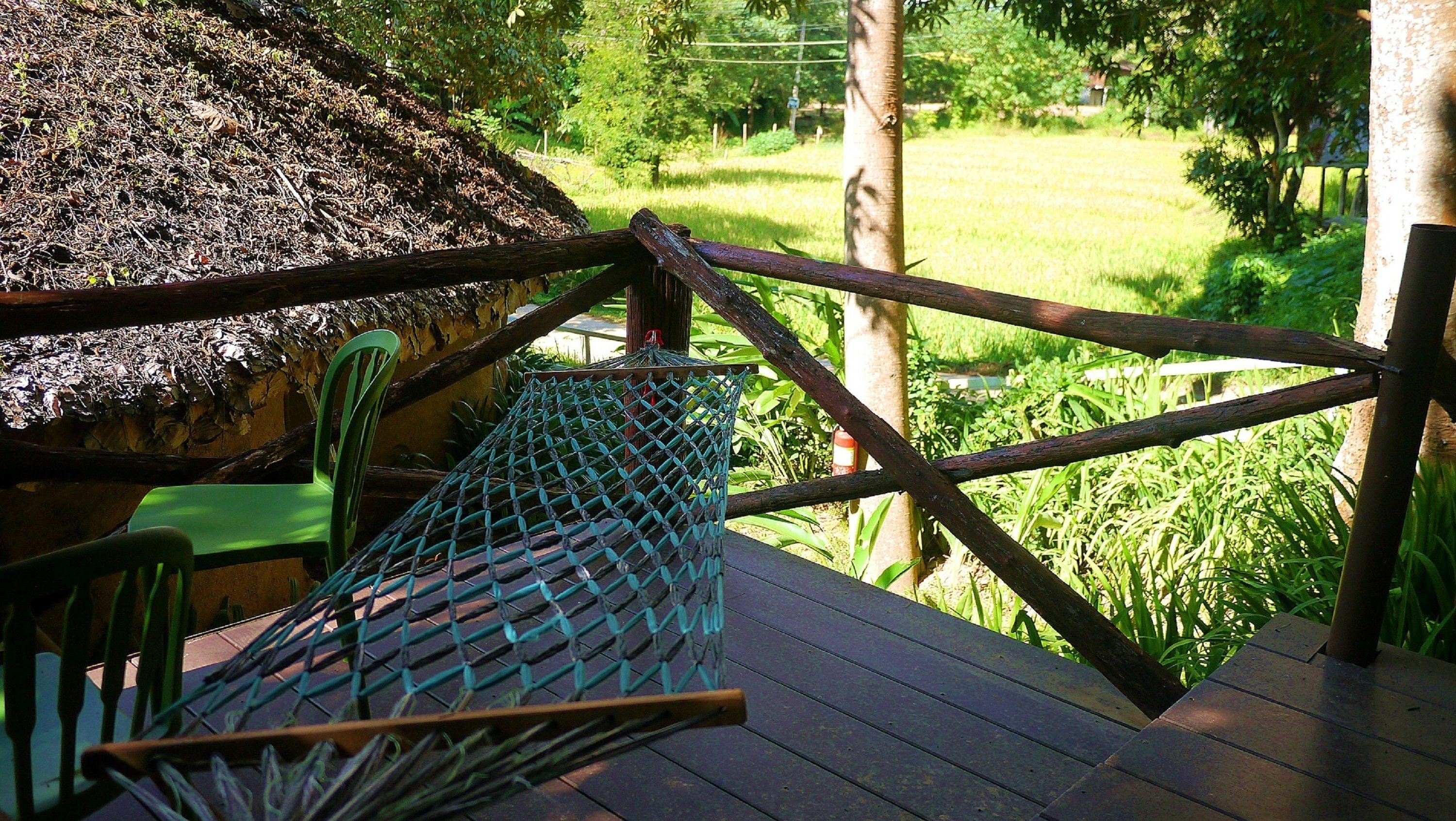 A wooden deck with a hammock, a thatched-roof structure, and a view of a green field.