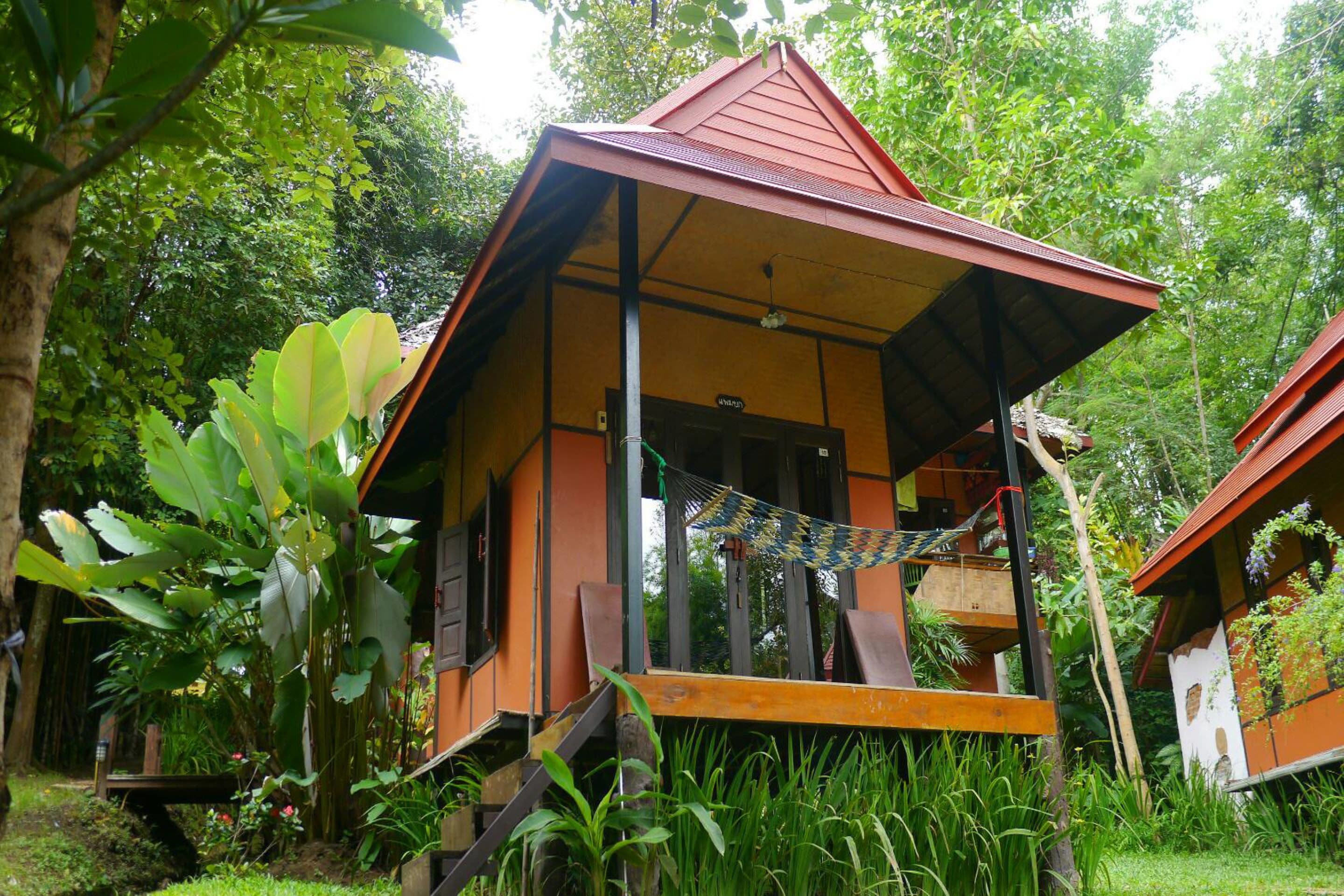 A rustic wooden structure with a sloped roof, surrounded by lush greenery and a hammock.