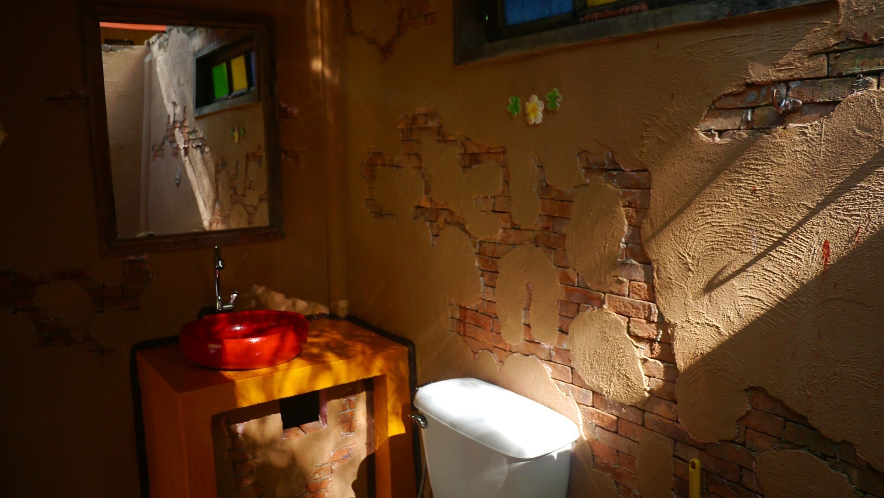 A bathroom with a brick wall, a red basin, and a toilet.
