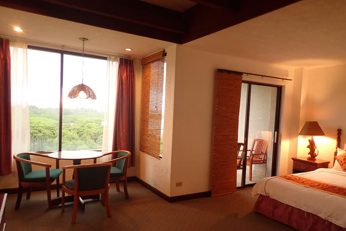 Habitación de hotel con comedor, cama y vista a zonas verdes.
