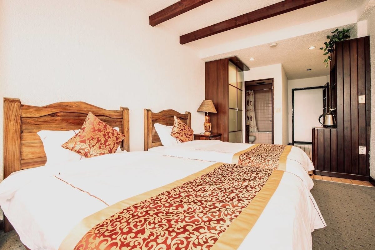Habitación de hotel con dos camas, cabeceros de madera y un corredor con estampado.