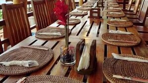 An outdoor dining area with wooden tables and chairs, arranged in a long row. - Cliffside View Hotel (Meyungs)