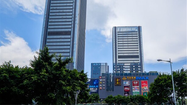 Deux gratte-ciel imposants aux façades vitrées réfléchissantes, entourés d’arbres et ornés de diverses enseignes commerciales.