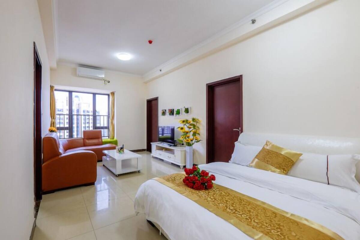 Habitación de hotel con cama, sofá, televisión y ventana con cortinas.