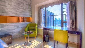 Une chambre d’hôtel moderne avec une grande fenêtre, un fauteuil vert, une chaise jaune, une petite table et un bureau.