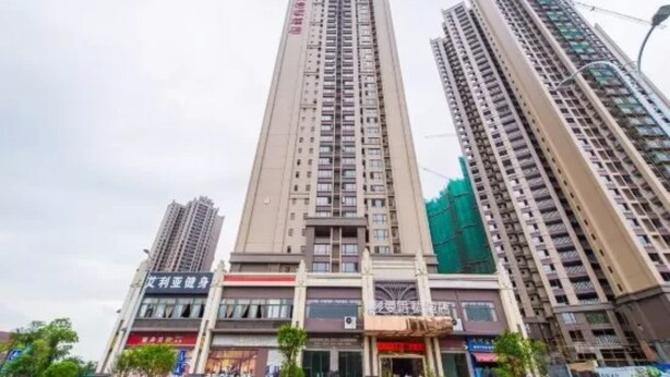 A high-rise building with multiple floors, featuring a central entrance with a covered area and several shops on the ground floor. - Guilin Manhattan Hotel North Station (Guilin)