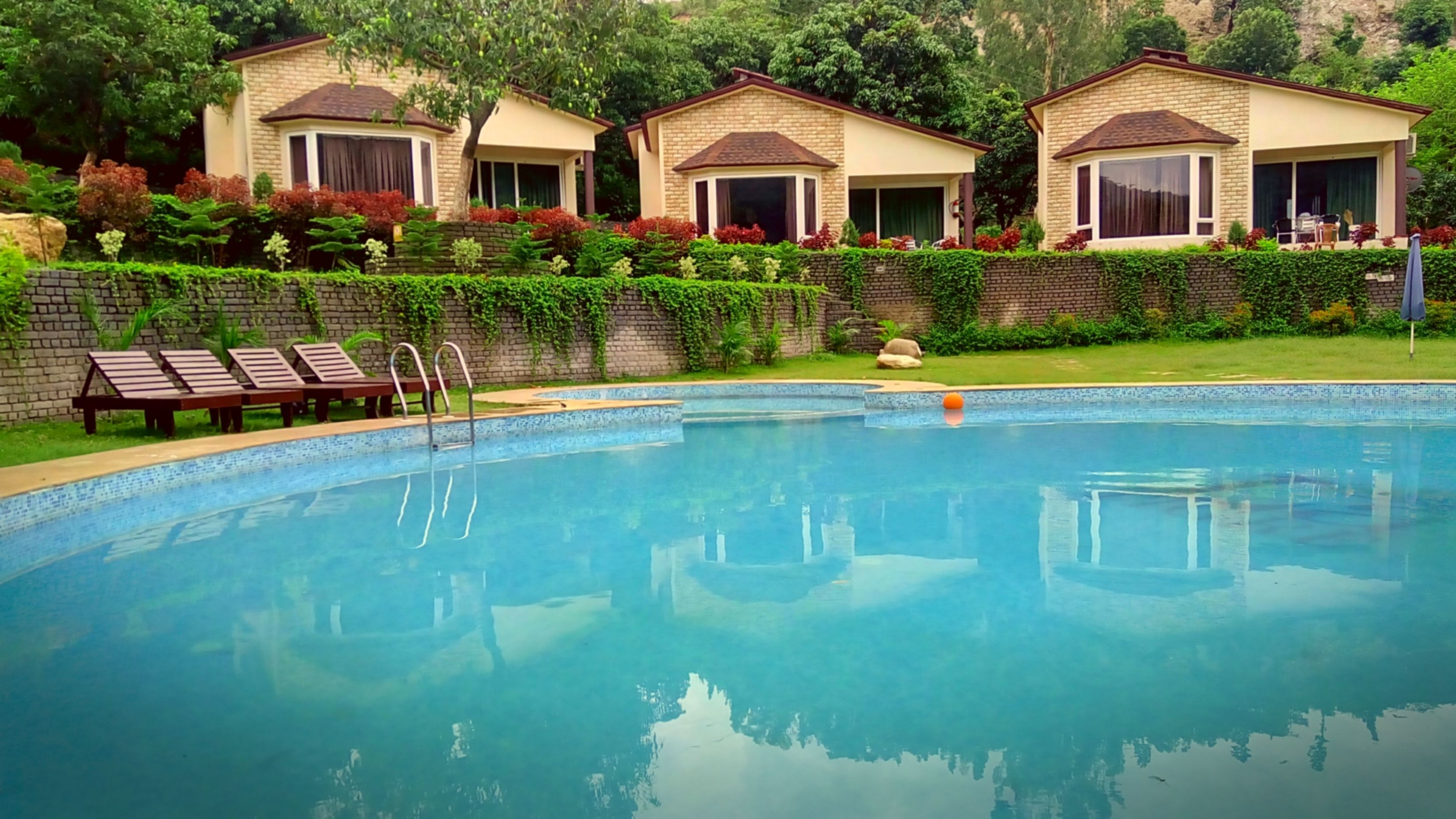 A swimming pool with lounge chairs and a brick wall with greenery.
