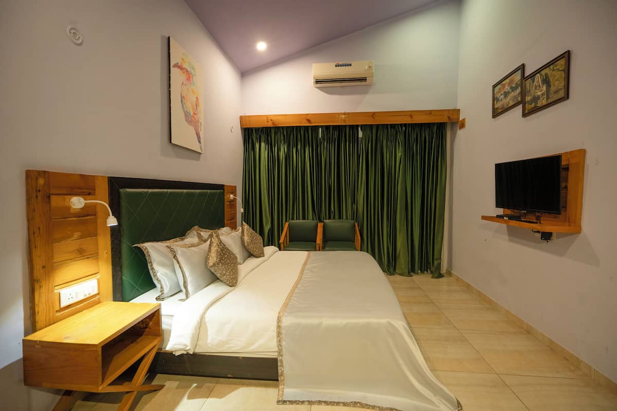 A neatly arranged bedroom with a bed, bedside table, green curtains, a mounted TV, and artwork on the walls.