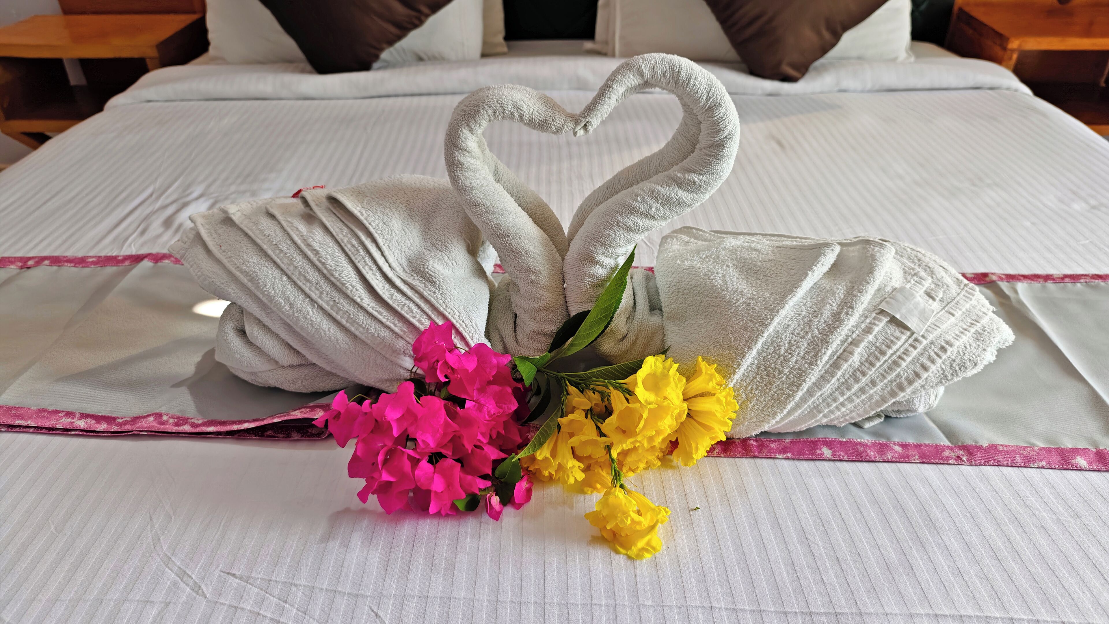 A bed with a heart-shaped towel arrangement and a bouquet of flowers.