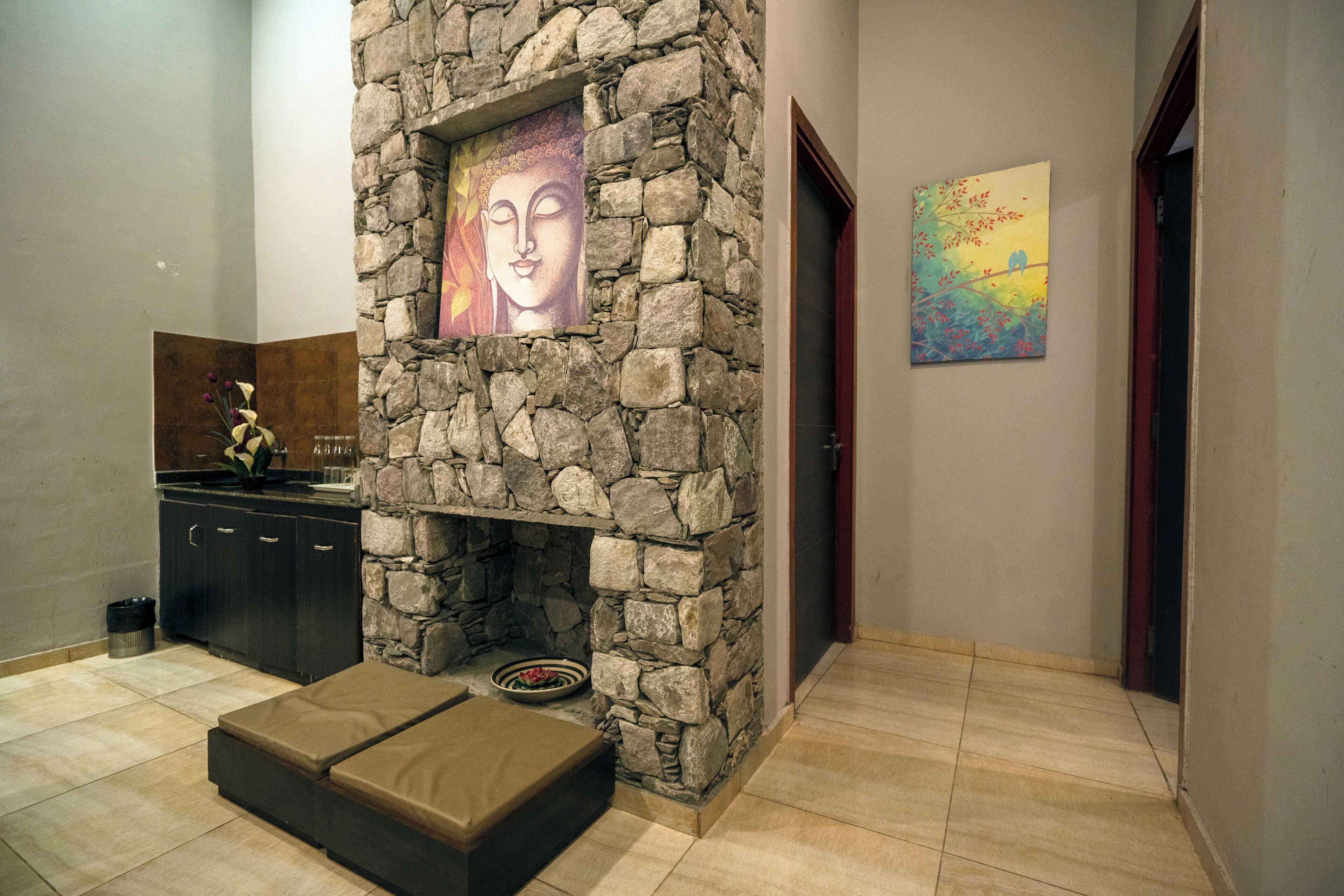 A stone fireplace with artwork, a cushioned bench, and a tiled floor in a hallway.