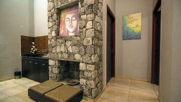 A stone fireplace with artwork, a cushioned bench, and a tiled floor in a hallway.