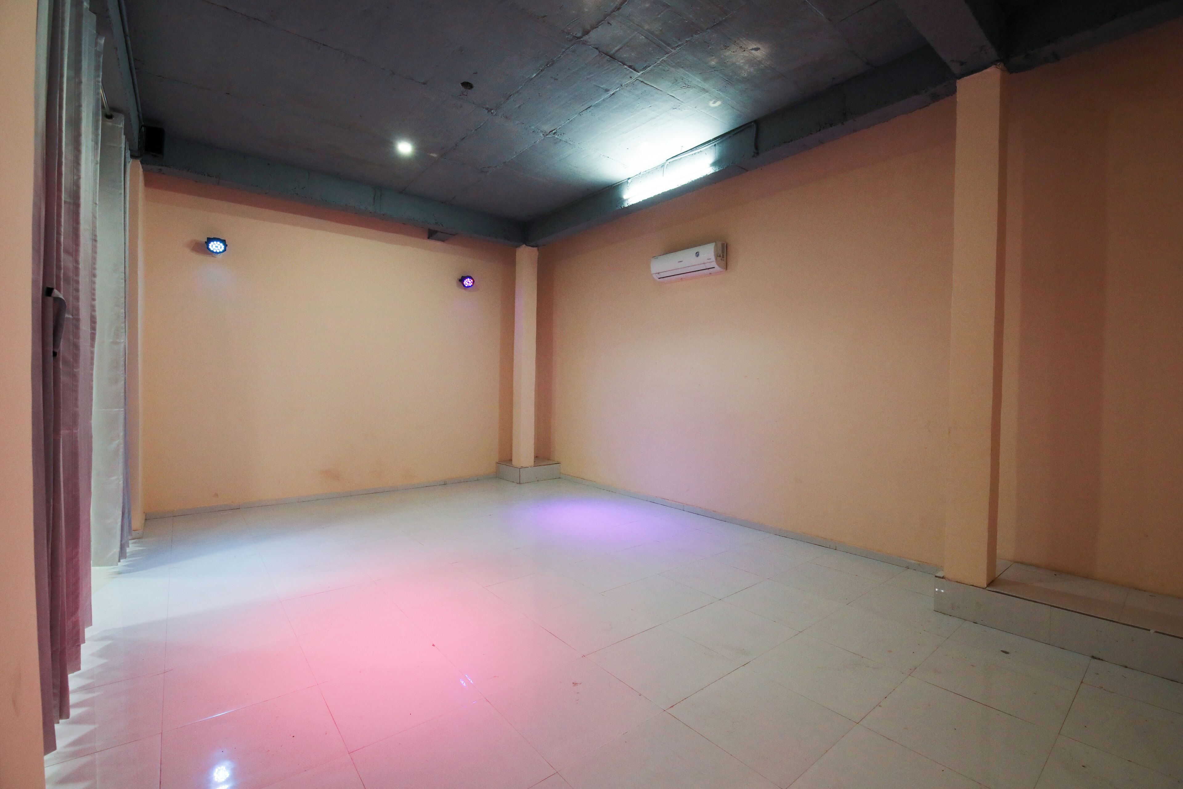 A room with a tiled floor, a ceiling with visible beams, and a wall-mounted air conditioning unit.