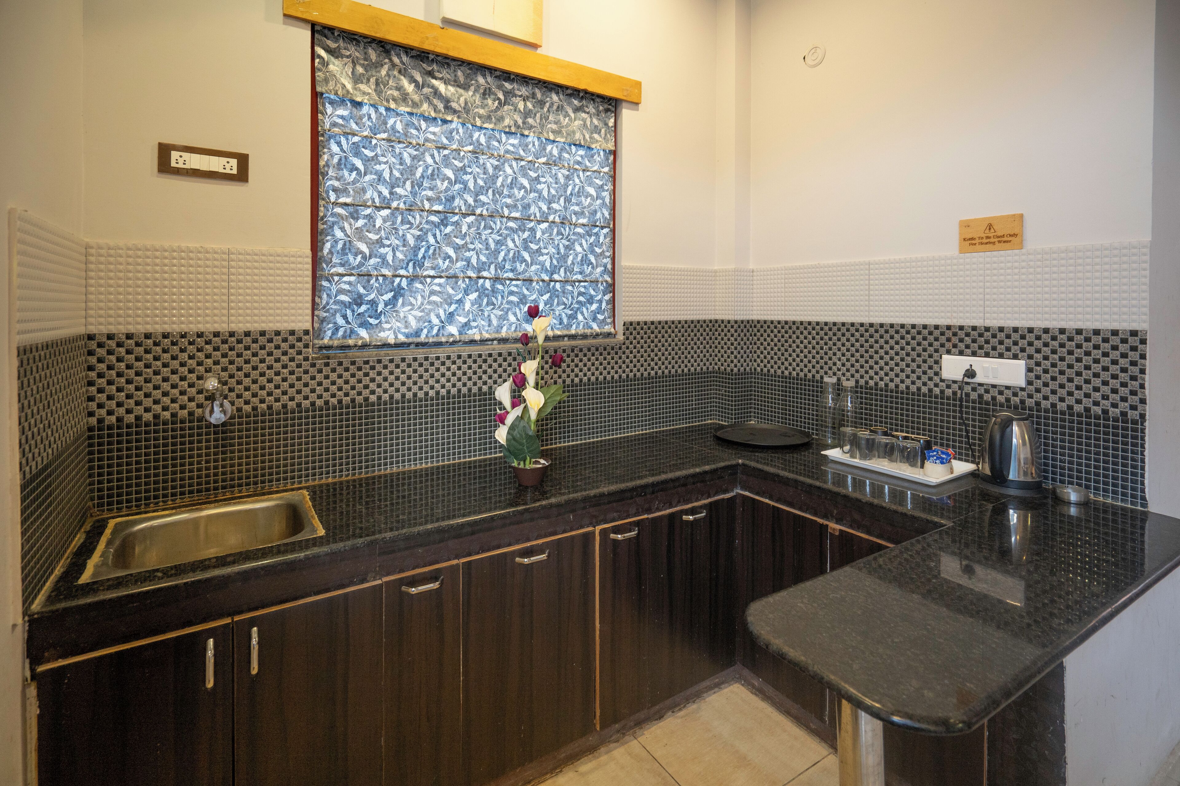Una cocina con armarios de madera oscura, una encimera negra, un lavamanos de acero inoxidable y un ventanal con vidrio de diseño azul.
