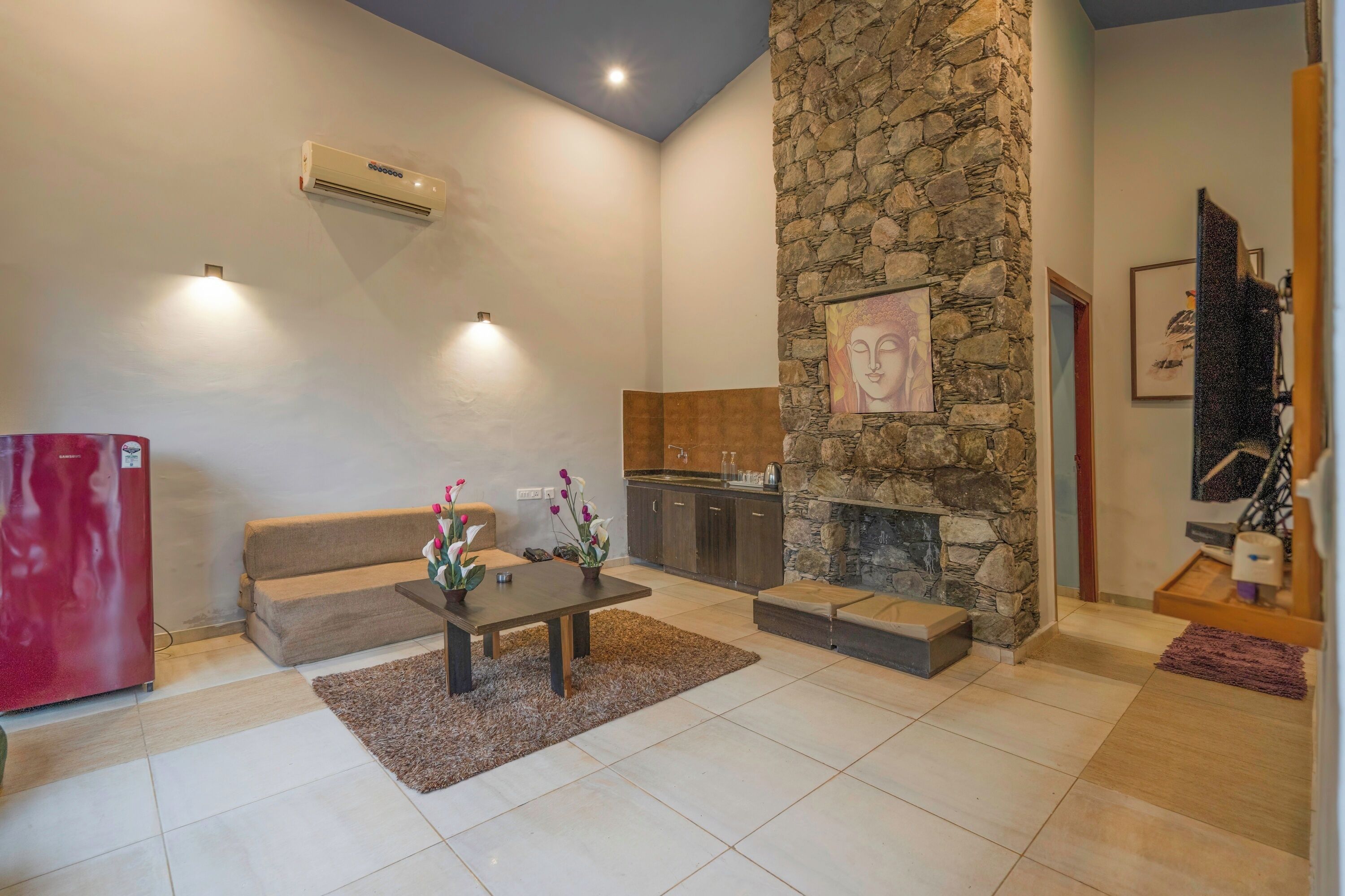 A modern living room with a stone fireplace, a kitchen area, and a red refrigerator.