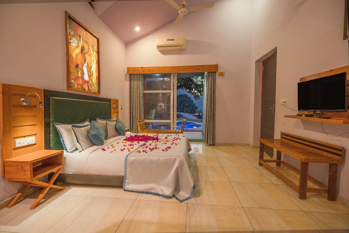 A hotel room with a bed, a wooden bench, a TV, and a painting on the wall.