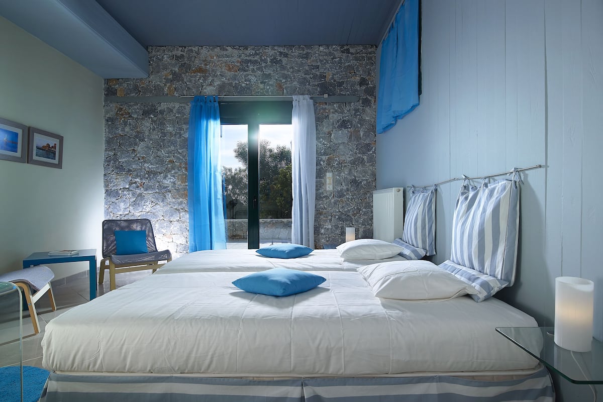 A bedroom with a large bed, a chair, a table, and a view of the outdoors through a glass door.