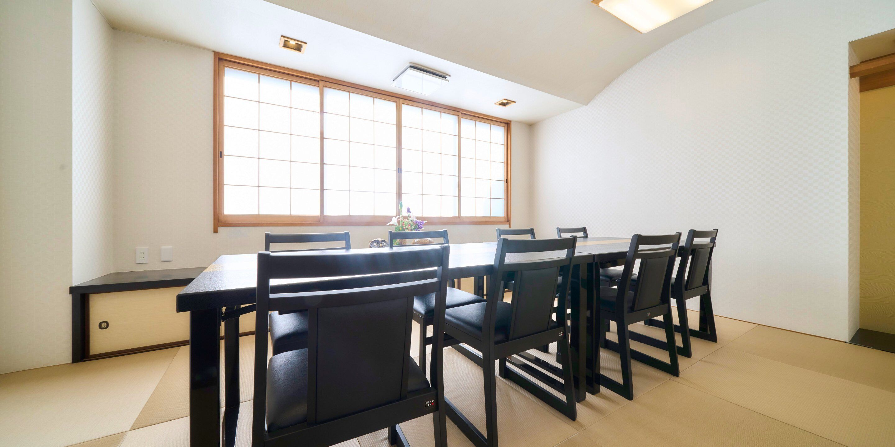 A dining area with a long table and six chairs, a window with wooden frames, and a ceiling light.