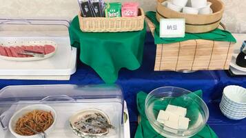 A buffet table with various food items and utensils, including a plate of sliced meat, a bowl of salad, and a container of tofu.