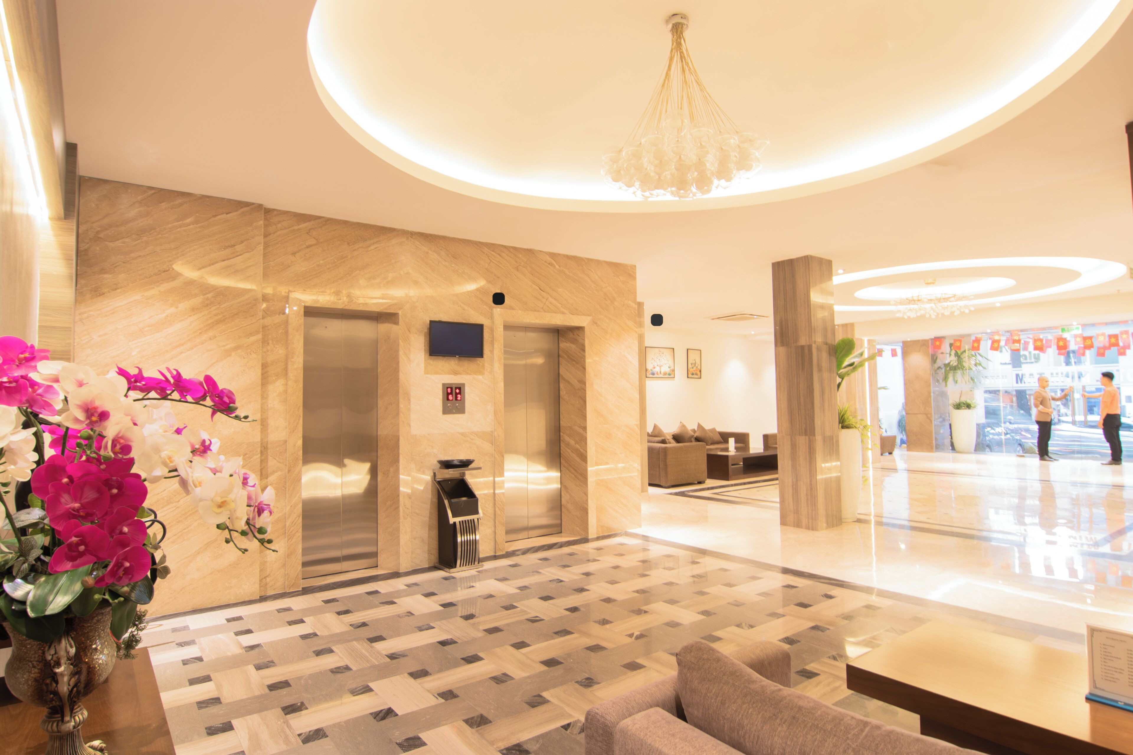 A lobby with a reception desk, a seating area, a chandelier, and a modern elevator.
