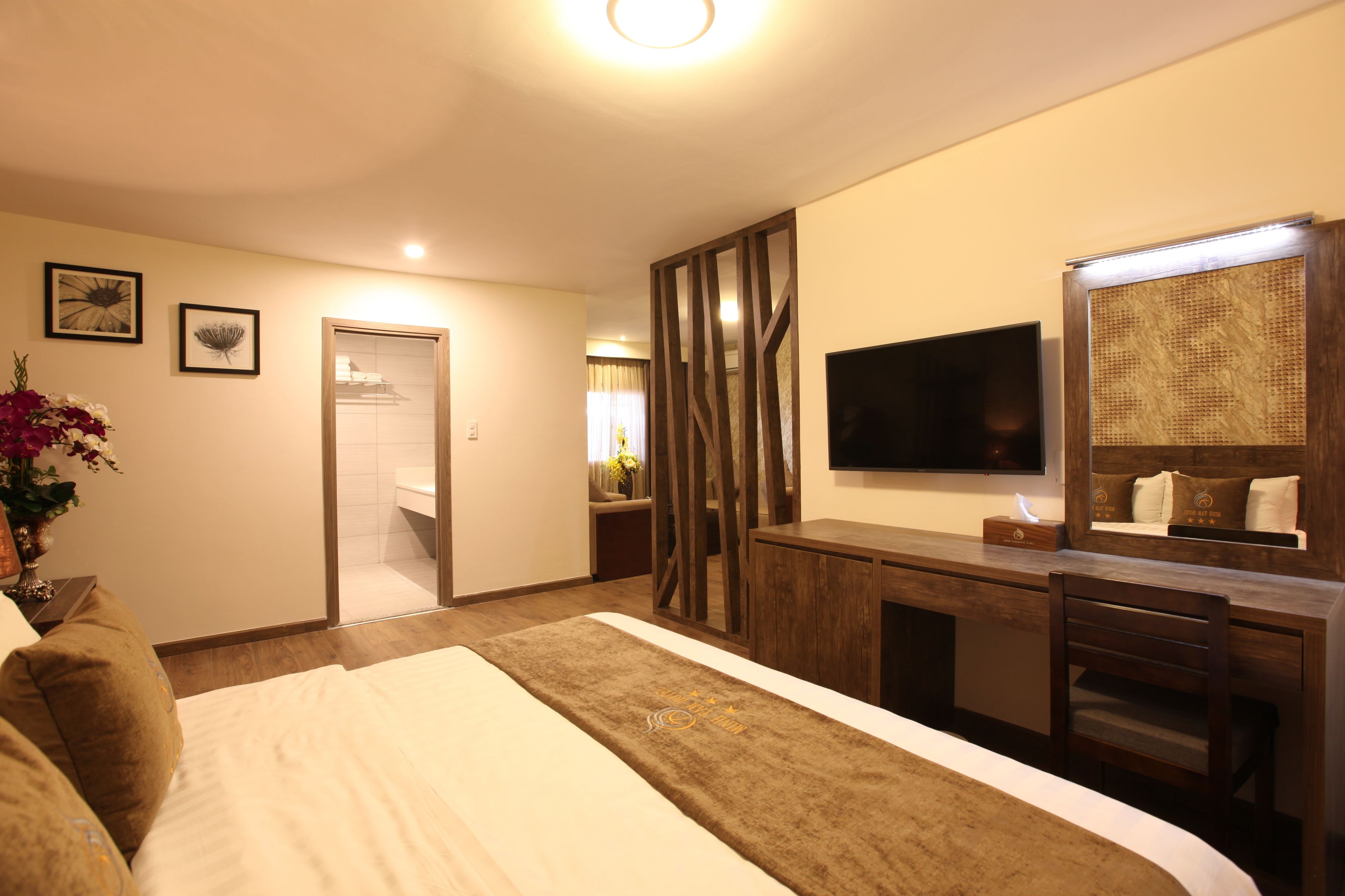 Une chambre d’hôtel avec un grand lit, un bureau avec un miroir, un téléviseur à écran plat et une salle de bain visible à travers une porte ouverte.