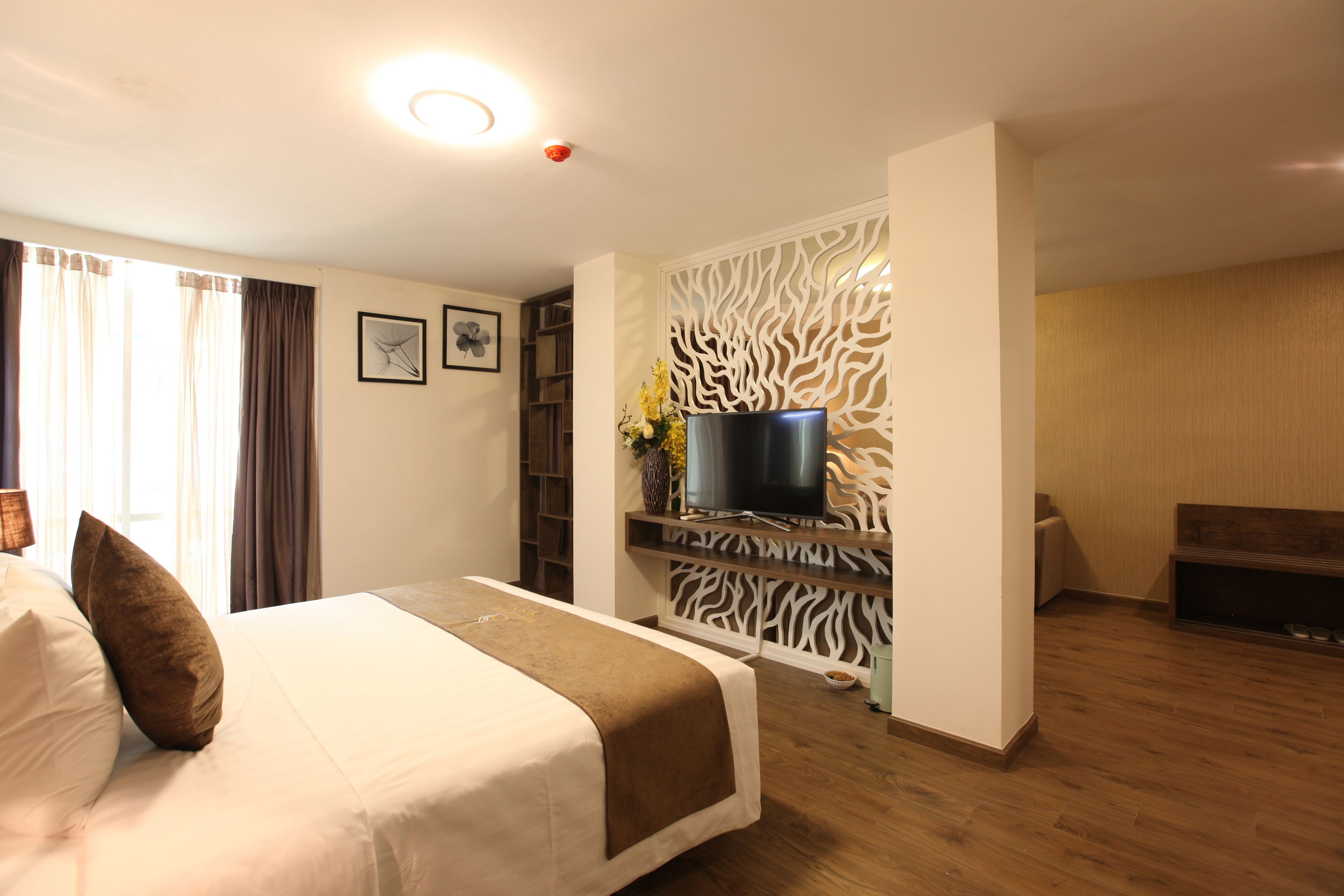 A hotel room with a bed, a television on a stand, a decorative wall panel, and a wooden floor.