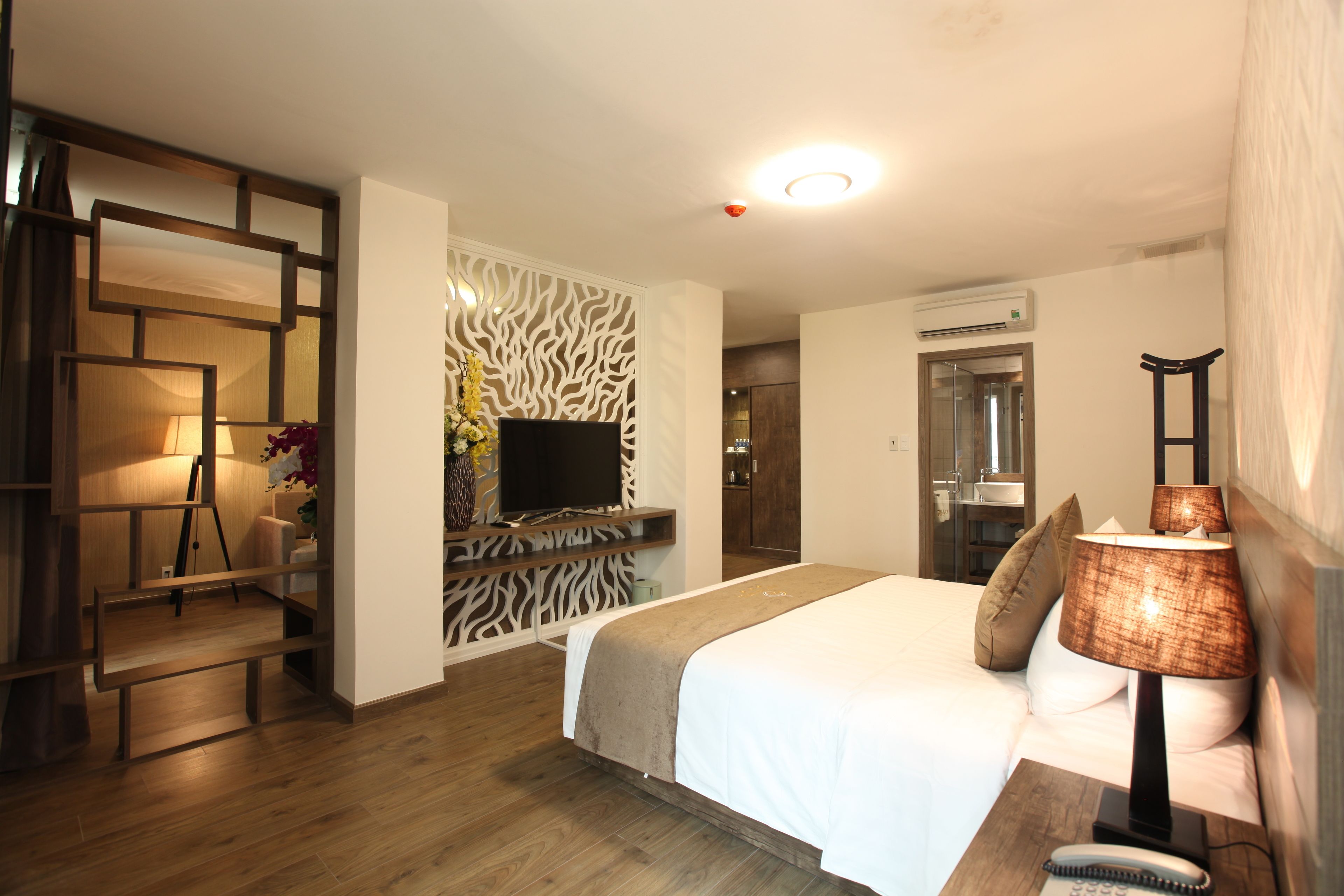 A hotel room with a bed, bedside table, lamp, TV, and a bathroom visible through an open door.