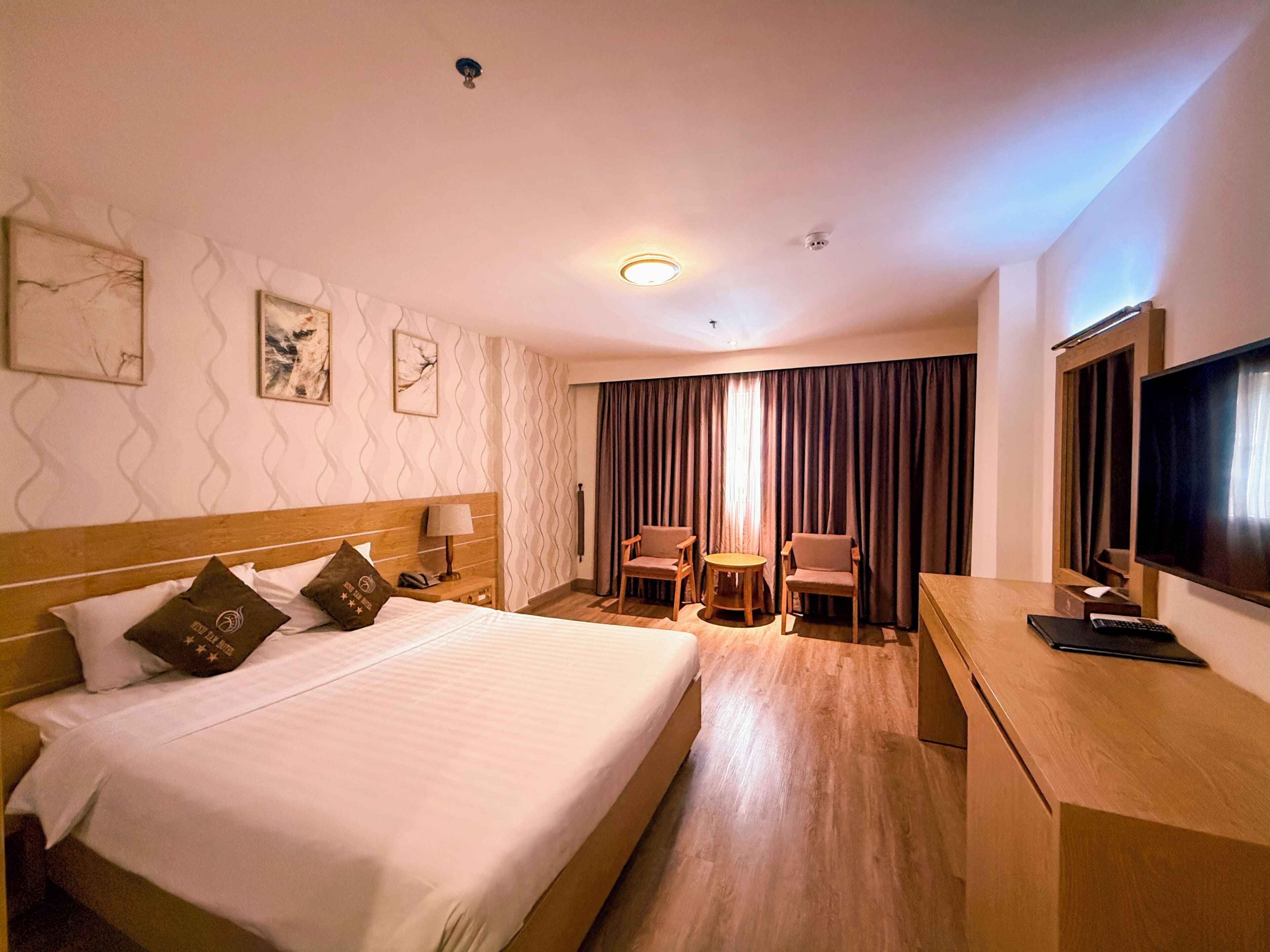 A hotel room with a large bed, a desk with a TV, a chair, and a small table.